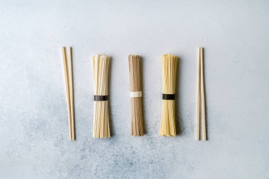 Different types of dry long asian noodles, chopsticks on light blue background