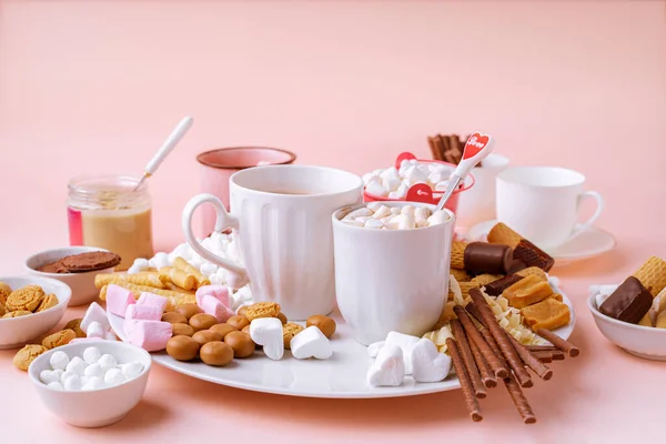 Horká čokoláda v hrncích, marshmallows, čokolády a sušenky na růžovém pozadí — Stock fotografie