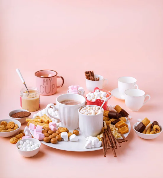 Ciocolată caldă în căni, sortimente de dulciuri de bezele, ciocolată și cookie-uri pe fundal roz — Fotografie, imagine de stoc