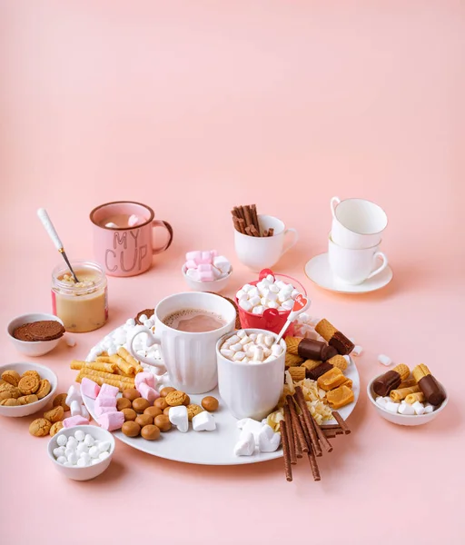 Forró csokoládé ital bögrék, édességek választéka mályvacukor, csokoládé és cookie-k rózsaszín alapon — Stock Fotó