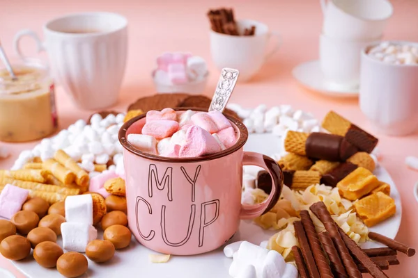 Horká čokoláda v růžovém hrnku, sladkosti sortiment marshmallows, karamely, čokolády a sušenky na růžovém pozadí — Stock fotografie