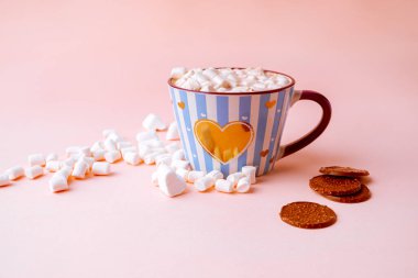 Şekerlemeli sıcak çikolata içeceği ve pastel pembe arka planda mavi çizgili fincanla çikolatalı cips. Yatay resim