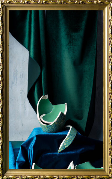 Stilllife with remnants of broken teal colored vase, emerald green and dark blue velvet, and picture frame. Portrait orientation