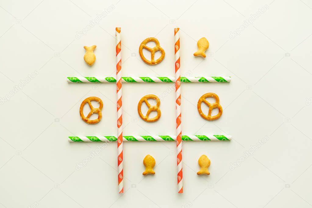 Tic-tac-toe game with small dry crackers and paper drinking straws on white background. Flat layout, horizontal image