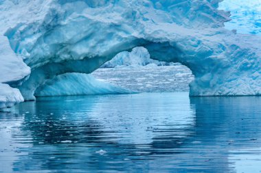 Snowing Floating Blue Iceberg Arch Reflection Paradise Bay Skintorp Cove Antarctica. Glacier ice blue because air squeezed out of snow. clipart