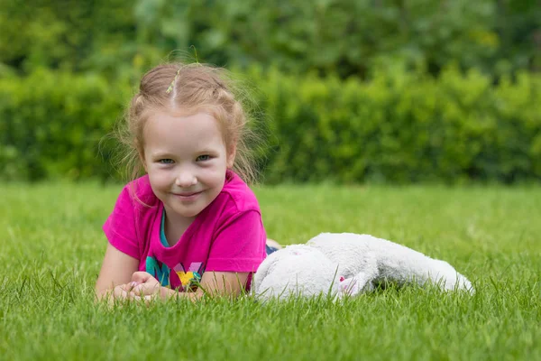 En 4 år gammal flicka som leker med ett gosedjur på gräset i en park — Stockfoto