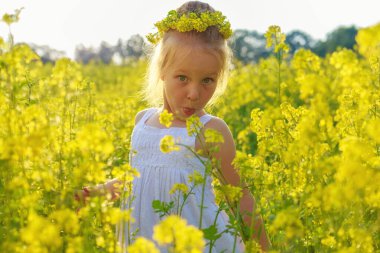 Küçük beyaz bir kız çiçek açan bir tecavüz çayırında oynuyor.