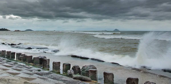 Stormy weather concrete coastline defence structure barrier with the ocean beyond and waves hitting the structure. With islands in the background set in the south china sea.