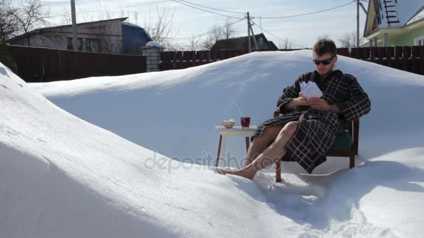 Молодой человек отдыхает на снегу и пьет сок — стоковое видео