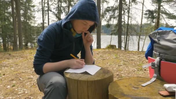 Flickan skriver anteckningar på stubben i skogen — Stockvideo