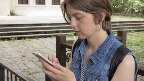 Chica joven mira el teléfono inteligente en el parque — Vídeos de Stock