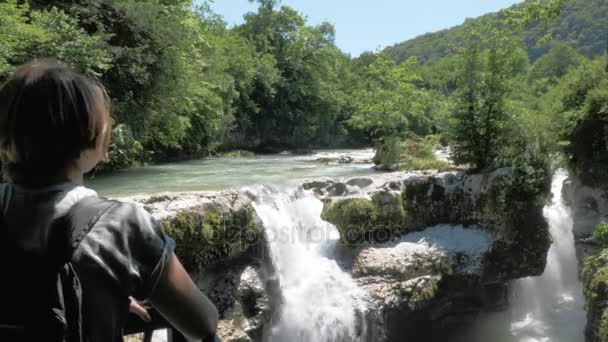Молодая девушка смотрит на небольшой водопад, Грузия, Мартвили — стоковое видео
