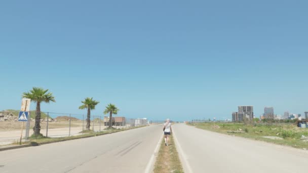 女の子の海岸線、バトゥミ、グルジアの空港の有刺鉄線のフェンスの近くの道路の上を歩く — ストック動画