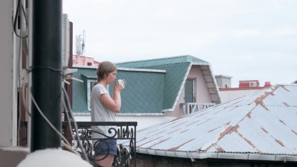 Νεαρή γυναίκα το πρωί, πίνοντας τσάι ή καφέ στο μπαλκόνι — Αρχείο Βίντεο
