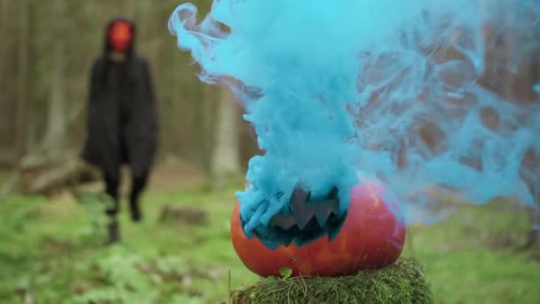 Osoba jde v masce a kabát v lese na Halloween s kouřovou dýní — Stock video