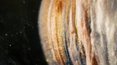 Altın mürekkep parçacıkları, siyah arkaplanda renkli bir kaos olarak suda akıyor.