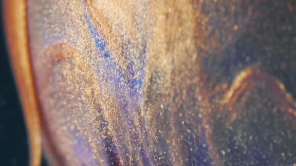 Частицы золотых чернил текут в воде как разноцветный хаос на черном фоне — стоковое видео