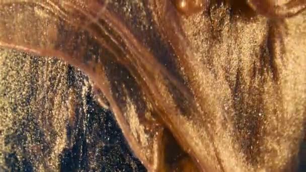 Particules d'encre dorée coule dans l'eau comme chaos coloré sur le fond noir 