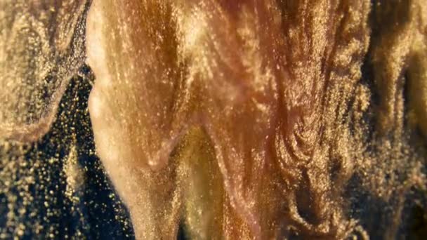 Particules d'encre dorée coule dans l'eau comme chaos coloré sur le fond noir 