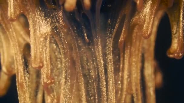 Gouden inkt deeltjes stromen in het water als kleurrijke chaos op de zwarte achtergrond — Stockvideo