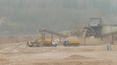 Bulutlu bir yaz gününde, yük makinası safra ocağında bir kamyona kum yüklüyor.