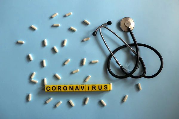 Stock image pills, stethoscope, thermometer, inhalation mask on a blue background with children`s yellow letters. Coronavirus 2019-nCoV disease and treatment concept.