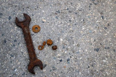 Büyük, paslı bir ingiliz anahtarı ve paslı cıvatalar, fındıklar ve yıkama makineleri gri noktalı taş bir yüzeye uzanıyor..