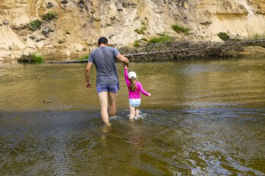 Baba ve kızı el ele tutuşup ormanın içinden nehrin diğer tarafına geçiyorlar. Bir aile su üzerinde yürür, su sıçratır..