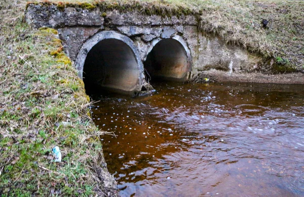 drainage pipes made of concrete under the road, to divert water during the spring flood. A strong stream of a forest stream, after a spring flood of a river, flows through concrete drainage pipes.