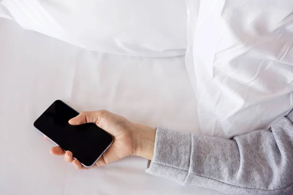 Arms holding mobile phone on bed