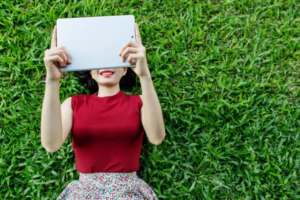 Happy woman lay down on grass with tablet