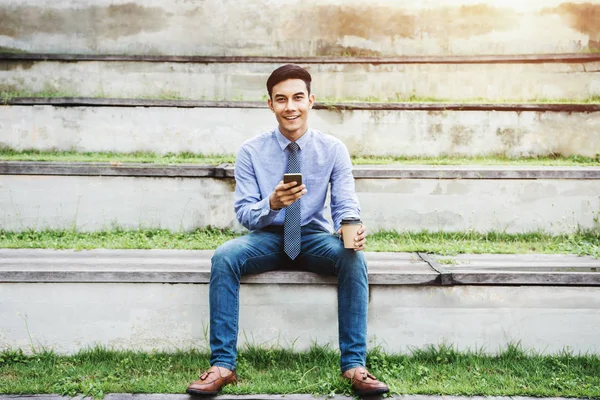 Empresario en ropa casual sentarse y utilizar un teléfono inteligente al aire libre par — Foto de Stock