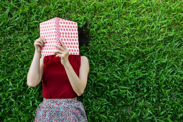 Lay γυναίκα κάτω είτε που χαλαρώνει στο πράσινο χορτάρι ανάγνωση βιβλίων το καλοκαίρι — Φωτογραφία Αρχείου