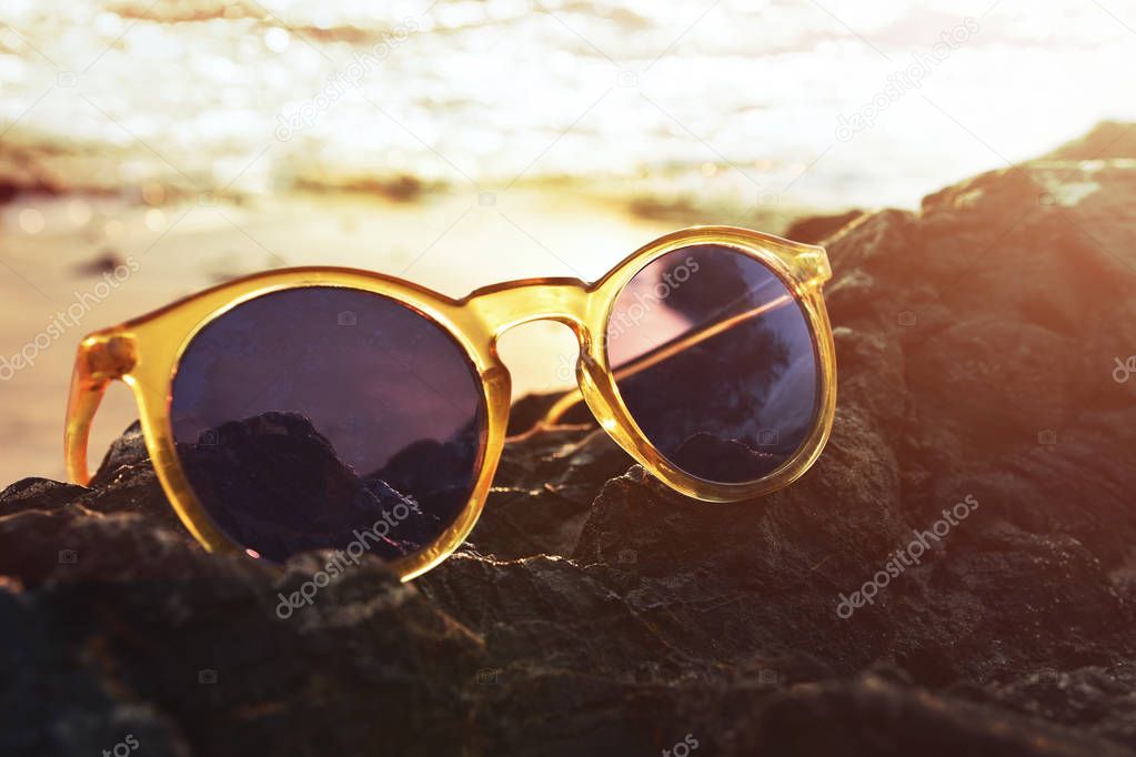 Closeup of sunglasses on island rock, Sunset sea as background, 
