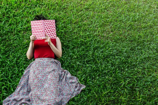 Nő feküdt le, vagy pihentető, a zöld fű olvasókönyv nyáron — Stock Fotó