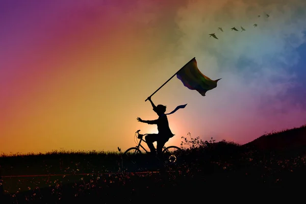 Свобода вираження думки гомосексуалістів, силует щасливої людини на велосипеді, тримання і підняття рук з прапором у райдужному сході сонця або заході сонця — стокове фото