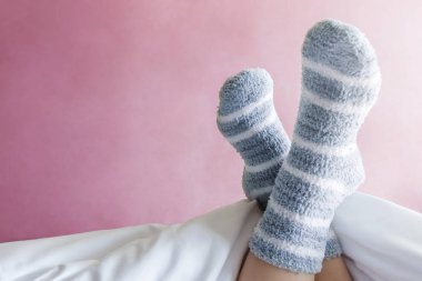 Relax and Cozy Concept, Female foot in Warm Stripe Wool Sock on Bed, Pink Pastel as background wall clipart