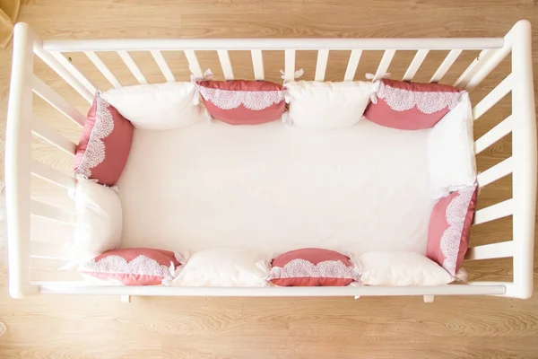 Łóżeczko dziecięce z białymi i burgundowymi poduszkami z koronkami — Zdjęcie stockowe