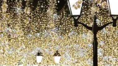Noel ve Yeni Yıl tatilleri geceleri şehir caddesinde açık aydınlatma. Klasik sokak ışıkları ile altın parıltı ve sallayarak çelenk.