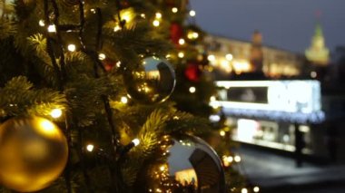 Moskova 'da tatiller. Meydanda bir Noel ağacı parıldıyor, toplarla süslenmiş ve güzel Noel oyuncakları yakın planda. Kremlin kulesi, yayalar ve gezginler bulanık arka planda yürüyor