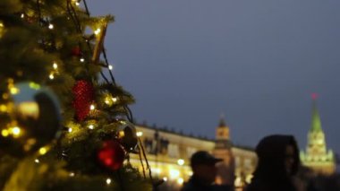 Moskova 'da tatiller. Meydanda bir Noel ağacı parıldıyor, toplarla süslenmiş ve güzel Noel oyuncakları yakın planda. Kremlin kulesi, yayalar ve gezginler bulanık arka planda yürüyor