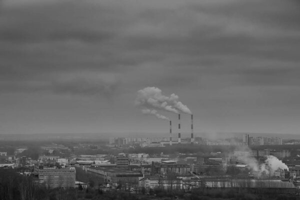 Dark smoke coming from the thermal power plant pipe.Factory smoke, polluting the atmosphere. Industrial zone in the city. Grey sky with overcast in winter day