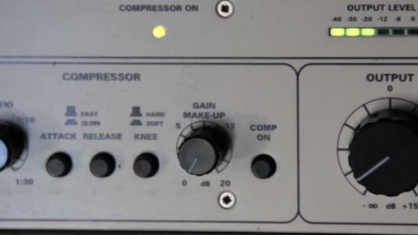 Un rack de compresseurs audio d'un système de renforcement sonore dans un studio d'enregistrement.L'ingénieur du son ajuste les pamètres avec des boutons. Les indicateurs de signal et de niveau sonore clignotent. 