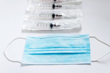 Beyaz arka planda kulaklık takan tıbbi bir maske. Sağlık uzmanları için tıbbi araçlar. Tek kullanımlık şırıngalar.