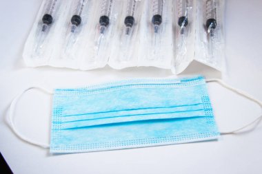 Beyaz arka planda kulaklık takan tıbbi bir maske. Sağlık uzmanları için tıbbi araçlar. Tek kullanımlık şırıngalar.