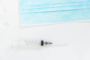 Beyaz arka planda kulaklık takan tıbbi bir maske. Sağlık uzmanları için tıbbi araçlar. Tek kullanımlık şırınga.