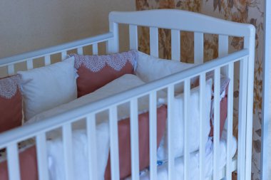 Akşamları bağcıklı beyaz ve bordo renkli yastıklı bebek yatağı. Uyku vakti. Mavi tonlu