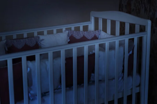 Beyaz ve bordo renkli yastıklı bebek yatağı. Gece geç saatte bağcıklı. Uyku vakti. Mavi koyu tonlar