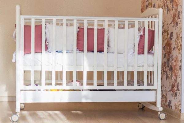 Beyaz ve Burgundy renkli bağcıklı bebek yatağı. Sabahları tekerlekler üzerinde pastel sarısı renklerle yatak odasında. Sert güneş ışığı pencereden gelir. Minimalist iç mekan.