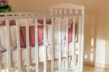 Beyaz ve Burgundy renkli bağcıklı bebek yatağı. Sabahları tekerlekler üzerinde pastel sarısı renklerle yatak odasında. Sert güneş ışığı pencereden gelir. Minimalist iç mekan.